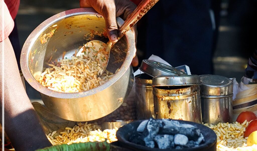 ndian street food vendor preparing spicy bhel puri snack with puffed rice, chutneys, and chopped vegetable