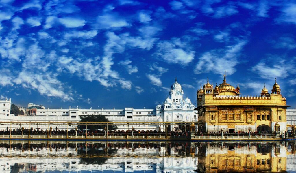 Golden Temple in Amritsar, India, reflecting in water under vibrant blue sky.