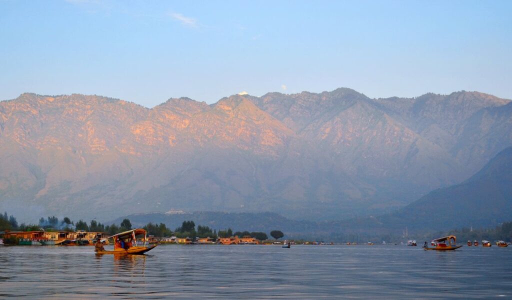 Traditional boats float on Dal Lake with mountain views at sunset in Kashmir, India.