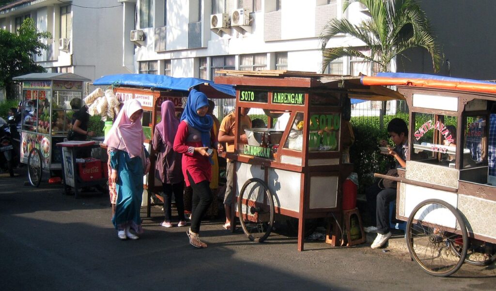 Street food carts in Indonesia with locals ordering dishes like Soto Ayam and Sate, set along a quiet residential street.