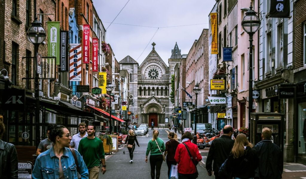 Busy street scene in Dublin, Ireland, with shops and historic church in the distance.