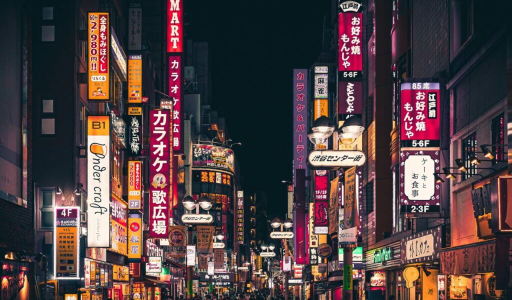 A vibrant street in Japan at night, filled with colorful neon signs and bustling shops.