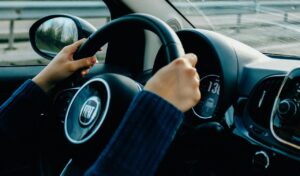Close-up of a person driving a Fiat car, holding the steering wheel with both hands positioned at 10 and 2, showcasing safe driving posture.