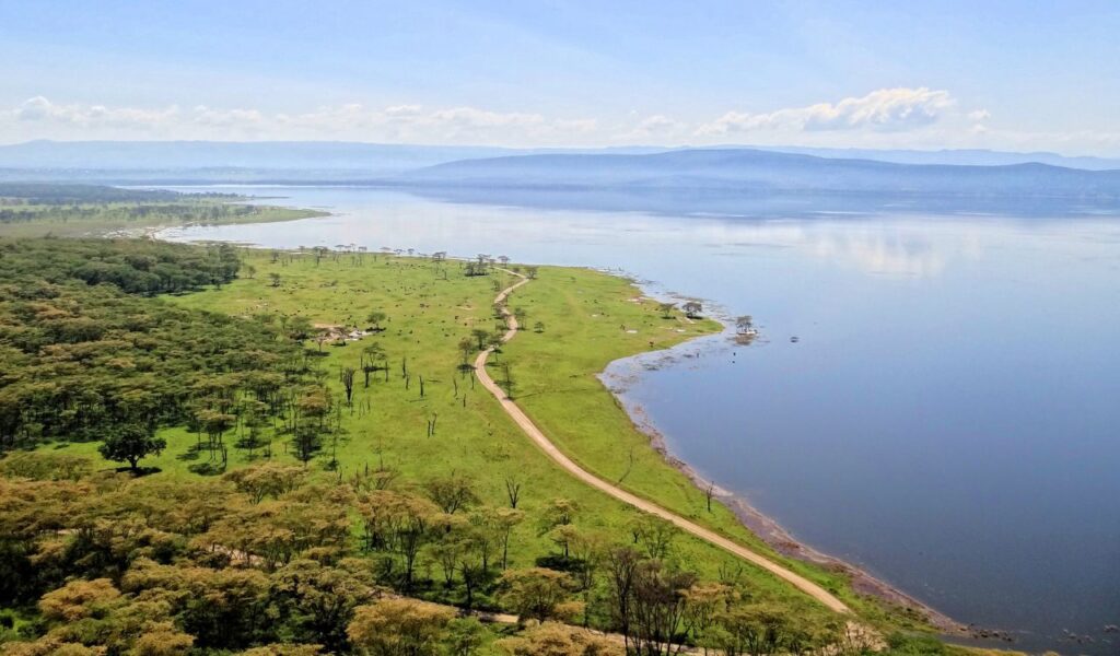Aerial view of Lake Nakuru in Kenya with lush green shores and calm reflective water.