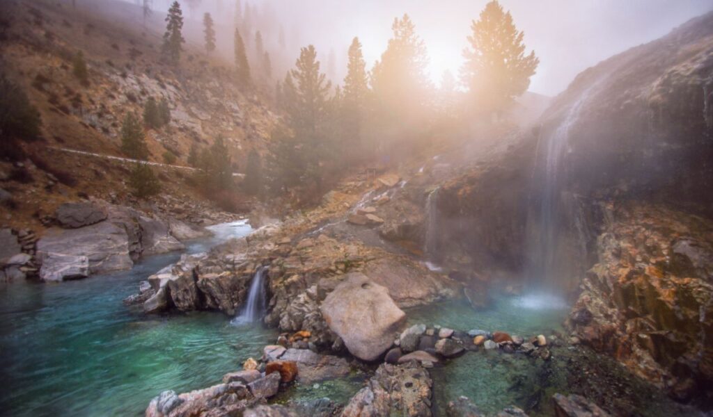 Kirkham Hot Springs with steaming pools, rocky cliffs, and misty forest backdrop.