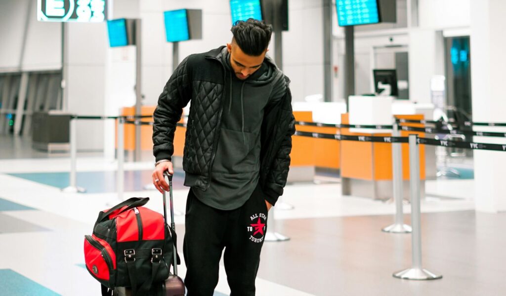 Man with luggage standing alone at airport check-in, looking down, possibly affected by a delayed or canceled flight.