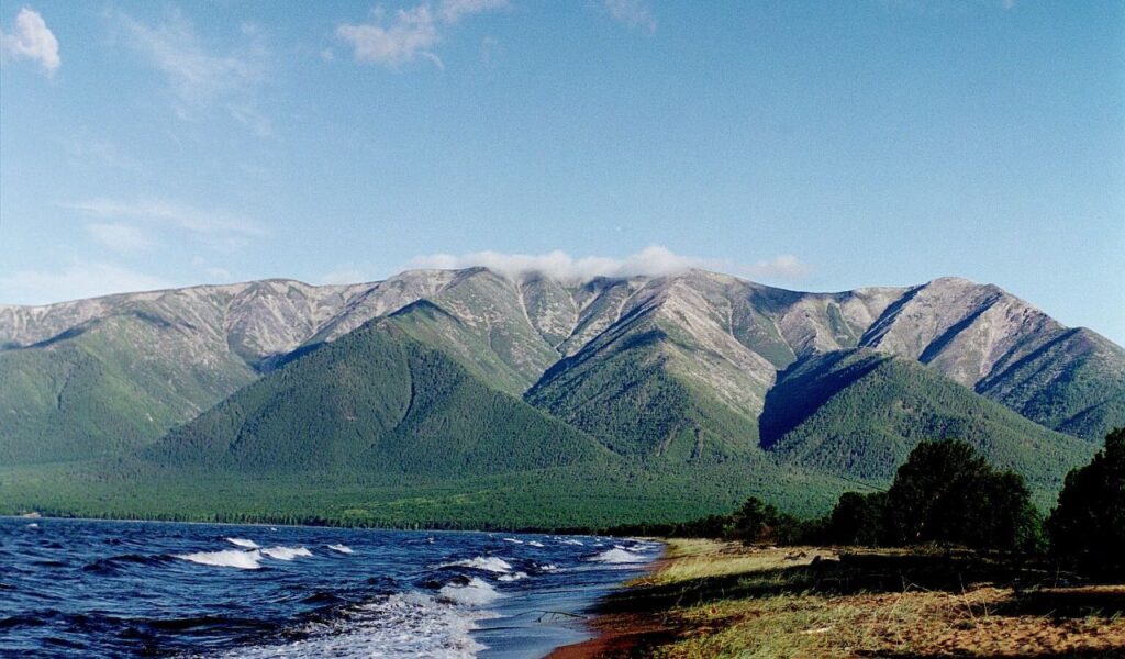 Lake Baikal shoreline with forested mountains under a clear blue sky in Russia.