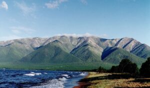 Lake Baikal shoreline with forested mountains under a clear blue sky in Russia.