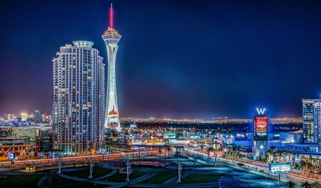 Night view of Las Vegas with the Stratosphere Tower illuminated, surrounded by high-rise buildings, casinos, and bright city lights.