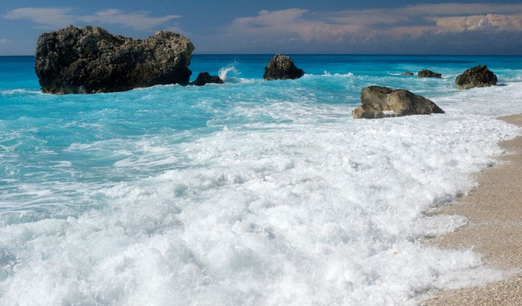 Waves crashing on a rocky shore with turquoise water, Lefkada Island, Greece.
