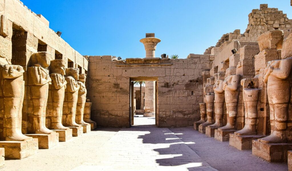 Luxor Temple in Egypt with rows of ancient statues and carved stone walls under a bright blue sky.