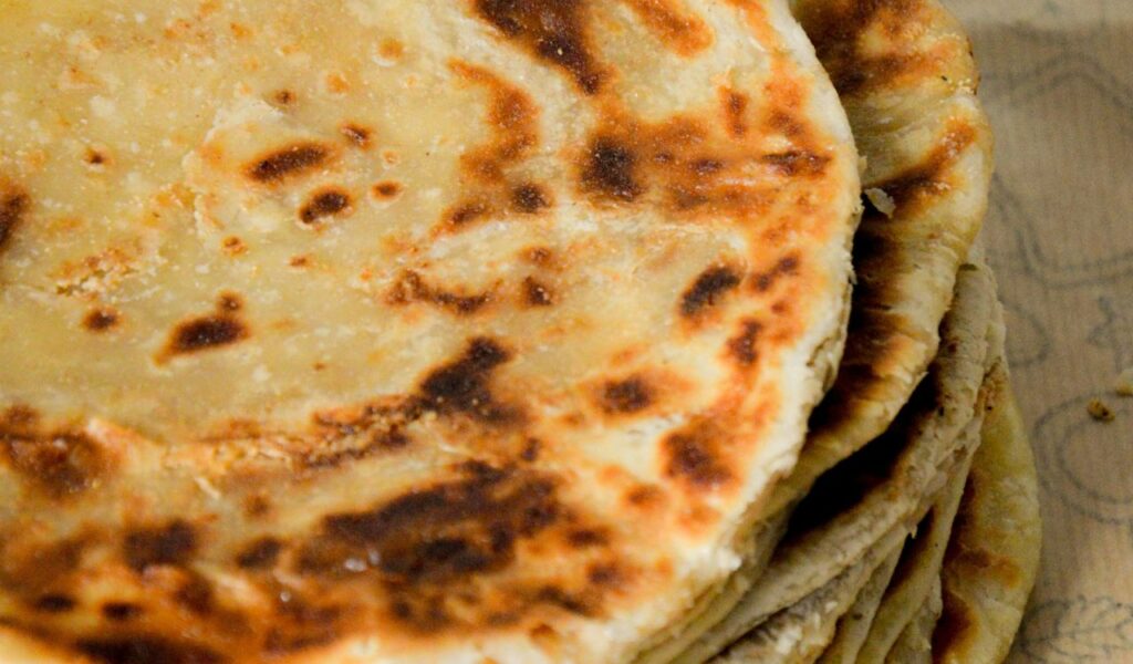 A close-up of a stack of golden-brown malawach flatbreads, showing their crispy, flaky texture.