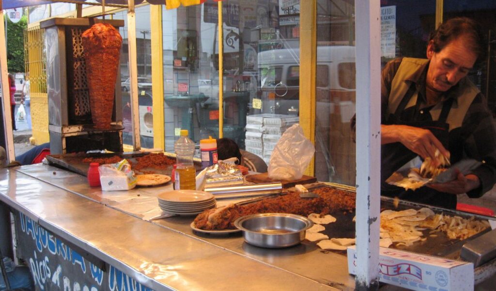 Street food vendor in Mexico preparing tacos al pastor with meat from a vertical spit at a local taqueria stand