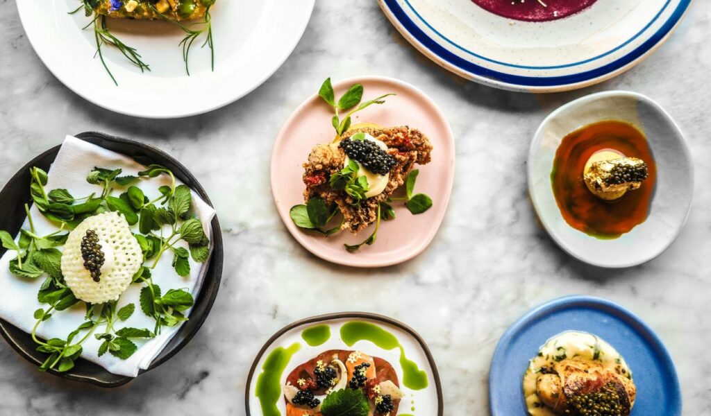 Assorted Michelin-starred dishes artfully plated with caviar, herbs, and sauces on colorful ceramic plates.