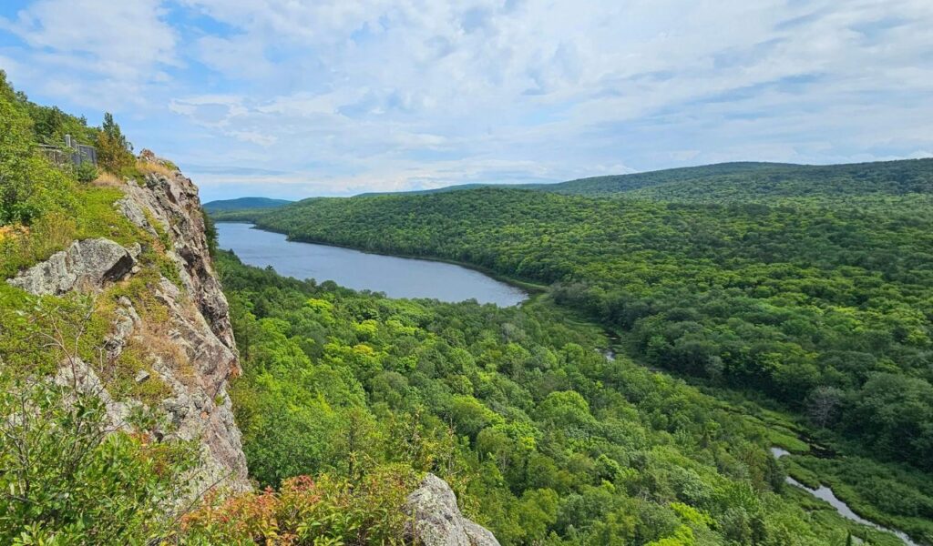 Scenic overlook in Michigan’s Upper Peninsula with rocky cliffs, a winding river, and dense green forest under blue skies.
