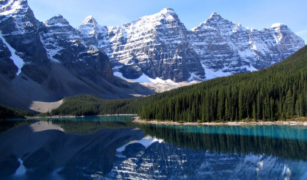Moraine Lake, Canada with clear water reflecting snowy mountains and forest.