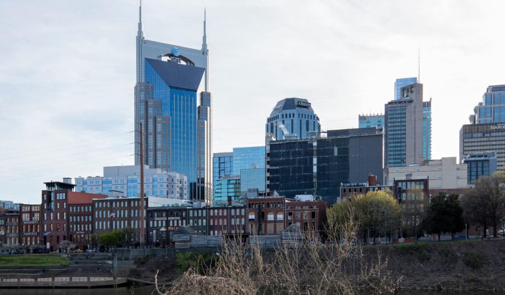 Skyline of Nashville, Tennessee, featuring the iconic AT&T Building and modern skyscrapers above historic brick buildings along the riverfront.