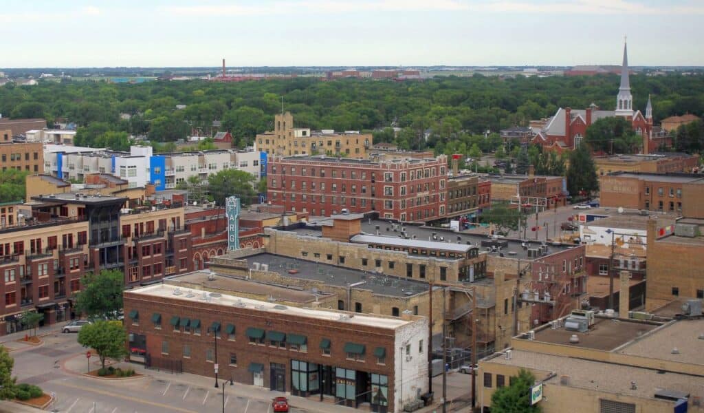 Downtown Fargo skyline with historic brick buildings, leafy trees, and the iconic Fargo Theatre marquee sign.