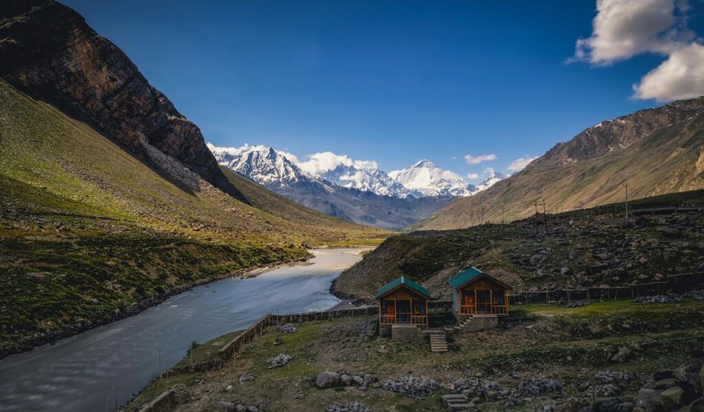 Remote cabins near a river in a mountain valley with snowcapped peaks and blue sky in North Sentinel Island, India.