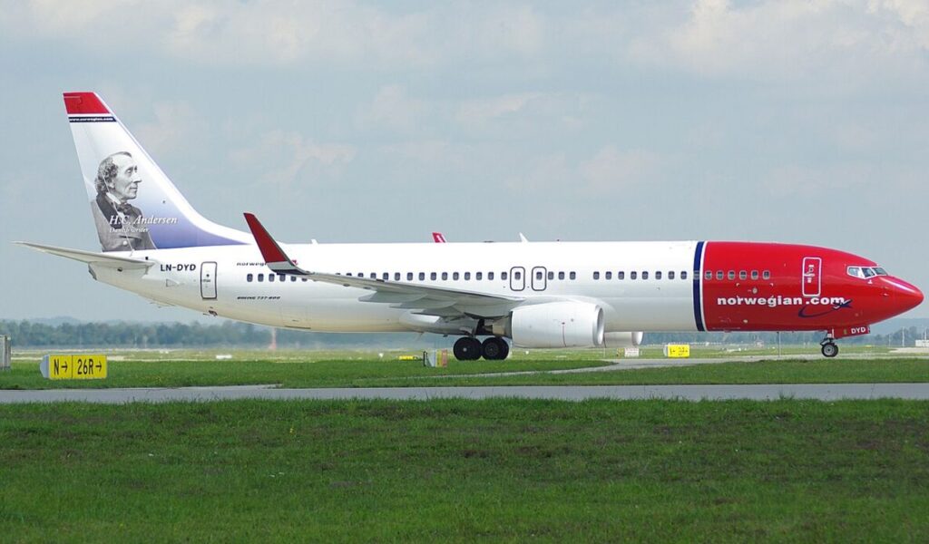 Norwegian Air Shuttle plane on runway, featuring Hans Christian Andersen’s portrait on the tailfin.