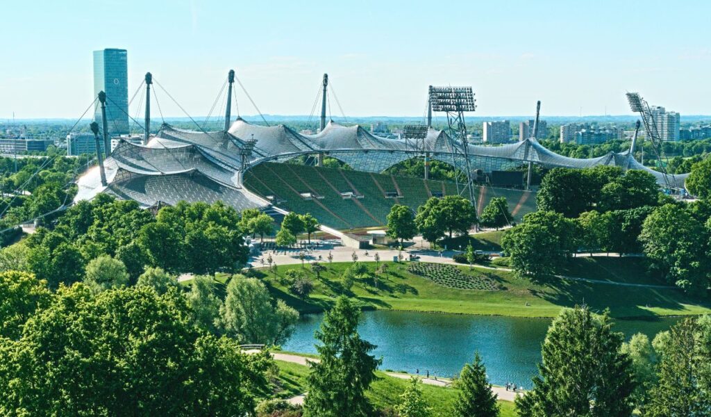 Aerial view of Munich’s Olympiapark, featuring the Olympic Stadium with its sweeping glass roof and surrounding greenery.