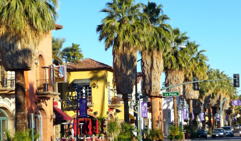 Colorful storefronts, towering palms, and sunlit charm—Palm Springs serving up desert cool on La Plaza.