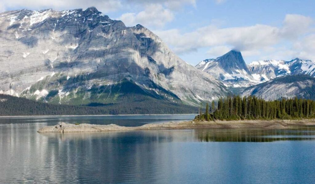 Snow-capped mountains reflect on the calm lake at Peter Lougheed Provincial Park in Alberta, Canada, on a clear day.