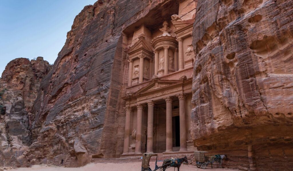 Petra in Jordan with its iconic rock-carved façade featuring columns and intricate details, set within towering sandstone cliffs.