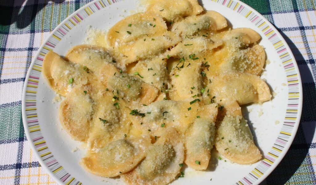 Plate of Polish pierogi dumplings topped with grated cheese and herbs, served on a striped rim plate over a checkered cloth.