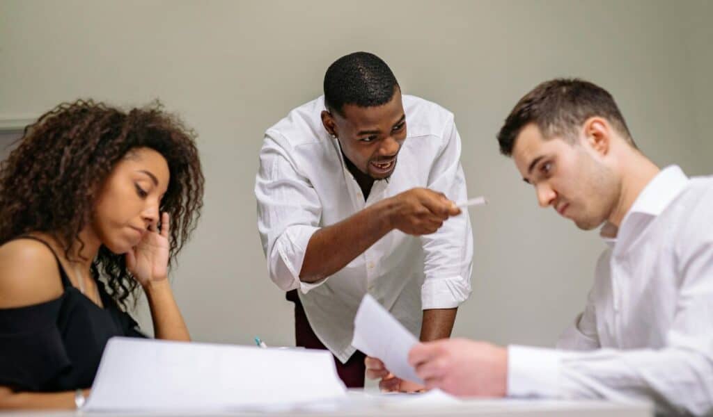 A man passionately argues with two colleagues during a serious discussion, reflecting tension and personal stakes in decision-making.
