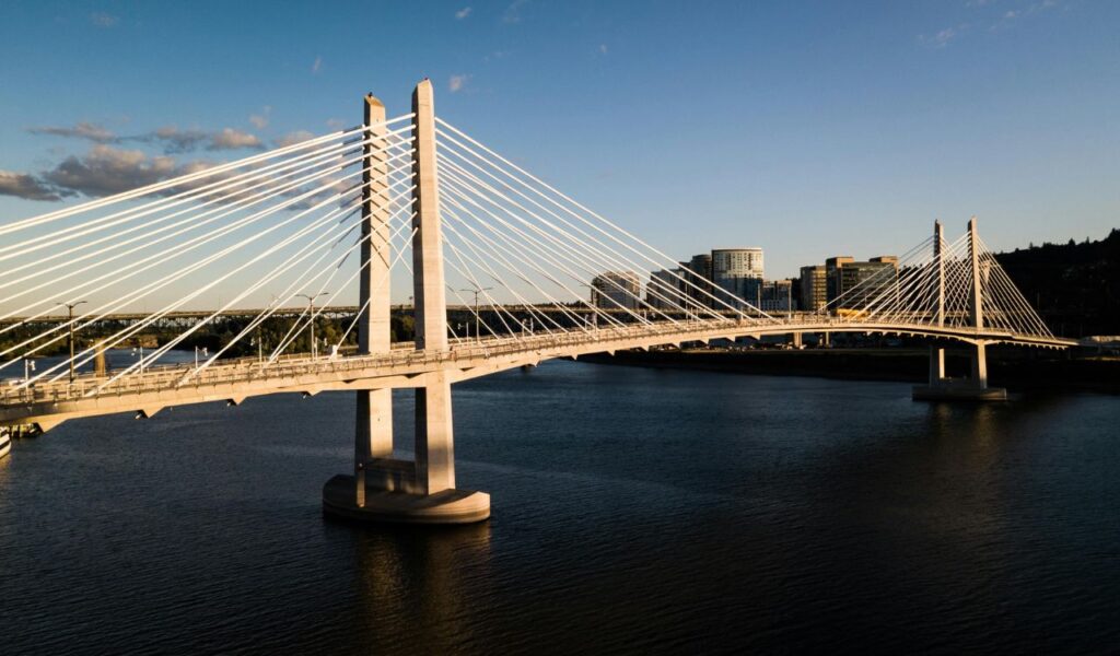 Tilikum Crossing bridge spans the Willamette River in Portland, Oregon, with cables glowing in the evening sunlight.
