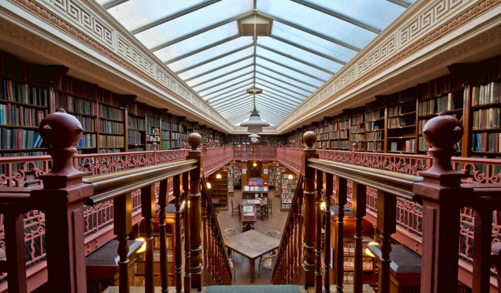Interior view of the Raphael Rooms with wooden railings, tall bookshelves filled with books, and a skylight ceiling illuminating the historic library space.