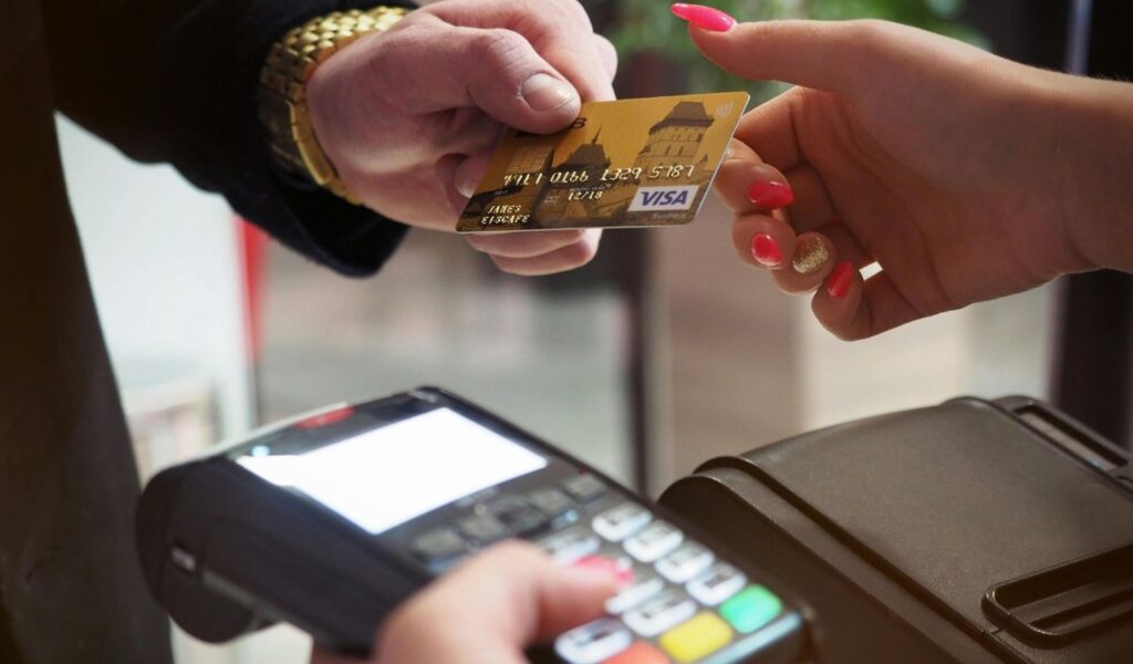 Close-up of a credit card being handed over for payment at a card terminal, with a coin also visible in hand.