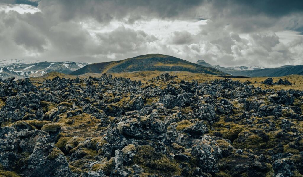 A rugged volcanic landscape covered in moss under dramatic cloudy skies, symbolizing resilience in a harsh, remote environment.