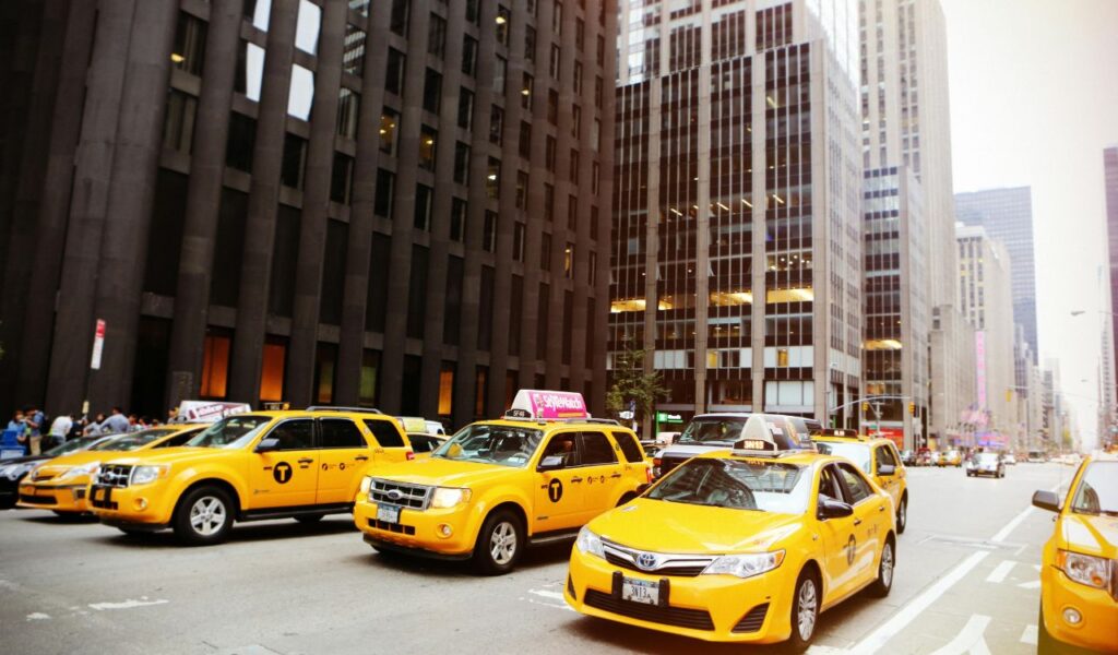 A row of yellow taxis in a busy city street surrounded by tall office buildings, symbolizing urban transportation and potential taxi-related scams.