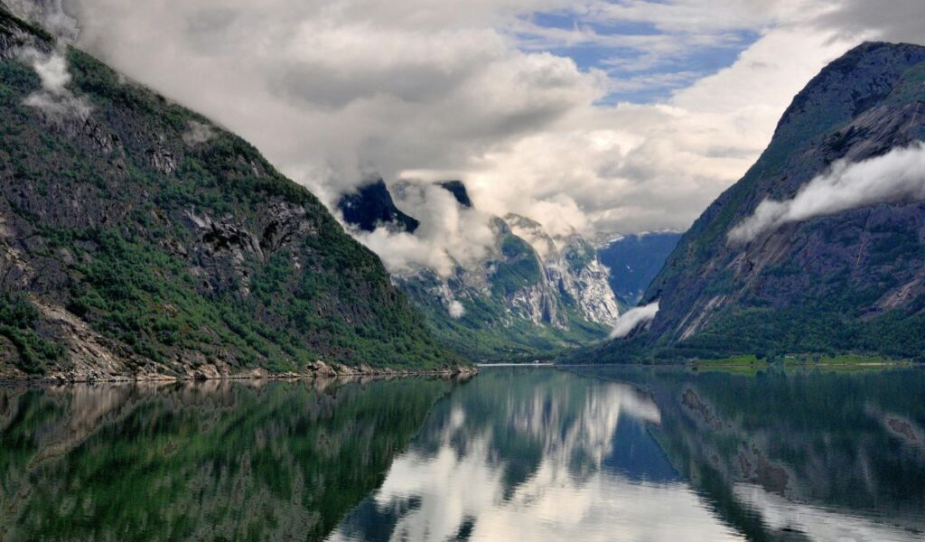 Moody clouds hang over steep cliffs and calm waters in Saguenay Fjord, reflecting the lush green mountains below.