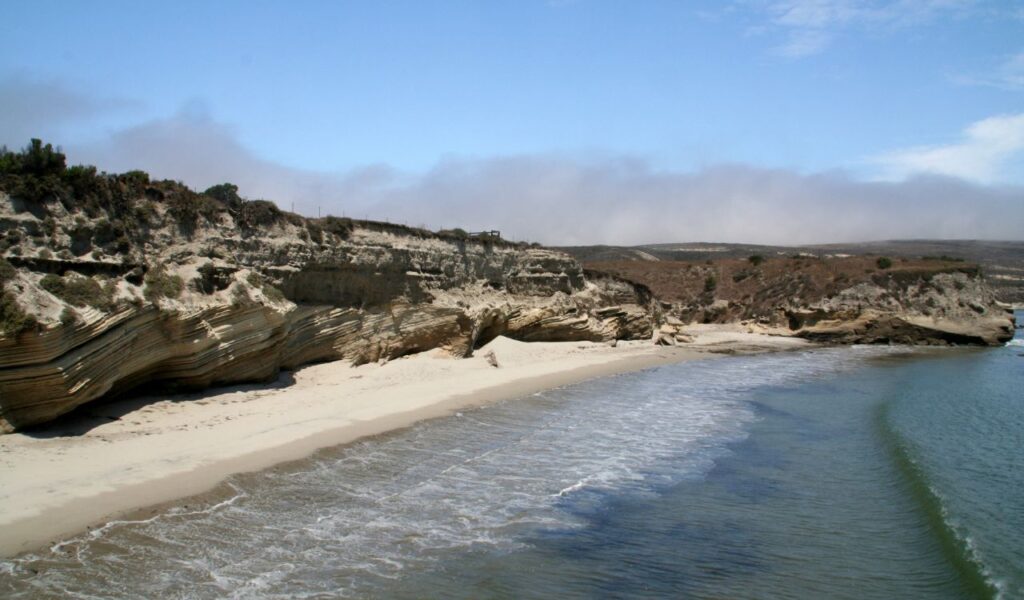 This is a view of Point Loma, located in San Diego, California. The beach features dramatic cliffs and gentle waves, offering a serene and picturesque coastline.