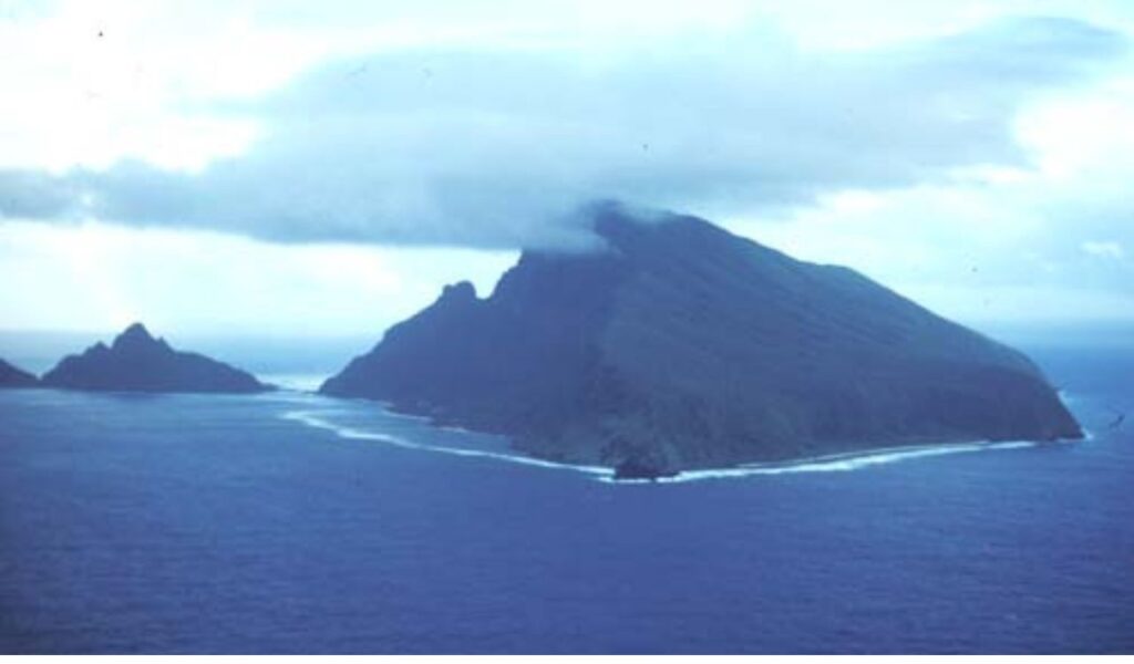 Dramatic volcanic island in Samoa surrounded by deep blue ocean, with peaks partly covered by low-hanging clouds.