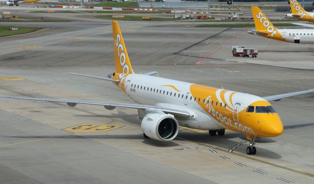 Scoot aircraft on the taxiway, featuring a bright yellow and white livery with bold flyscoot.com branding.