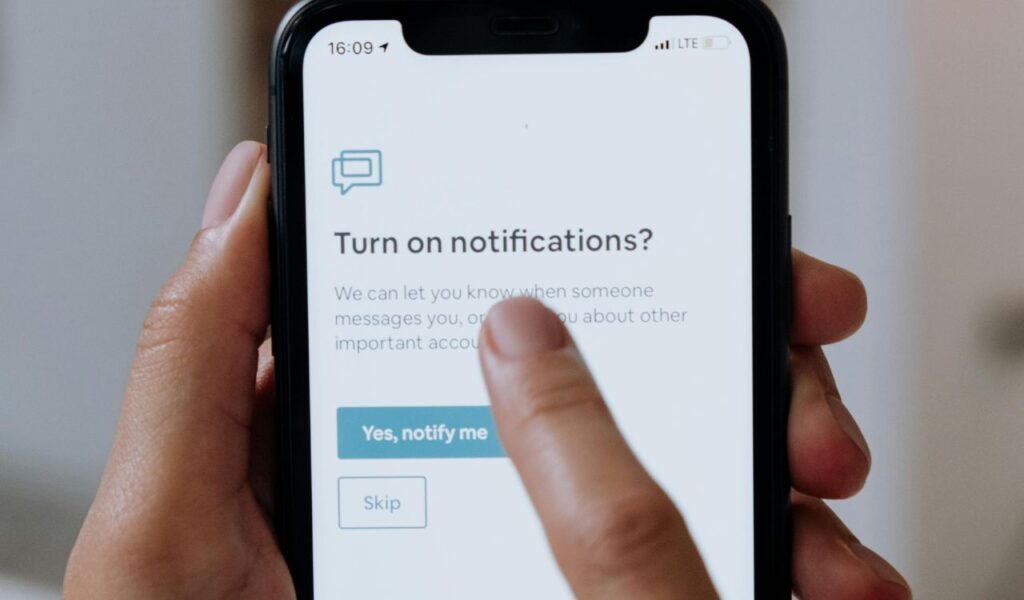 Close-up of a smartphone screen showing a notification opt-in prompt, with a hand about to tap “Yes, notify me” option.