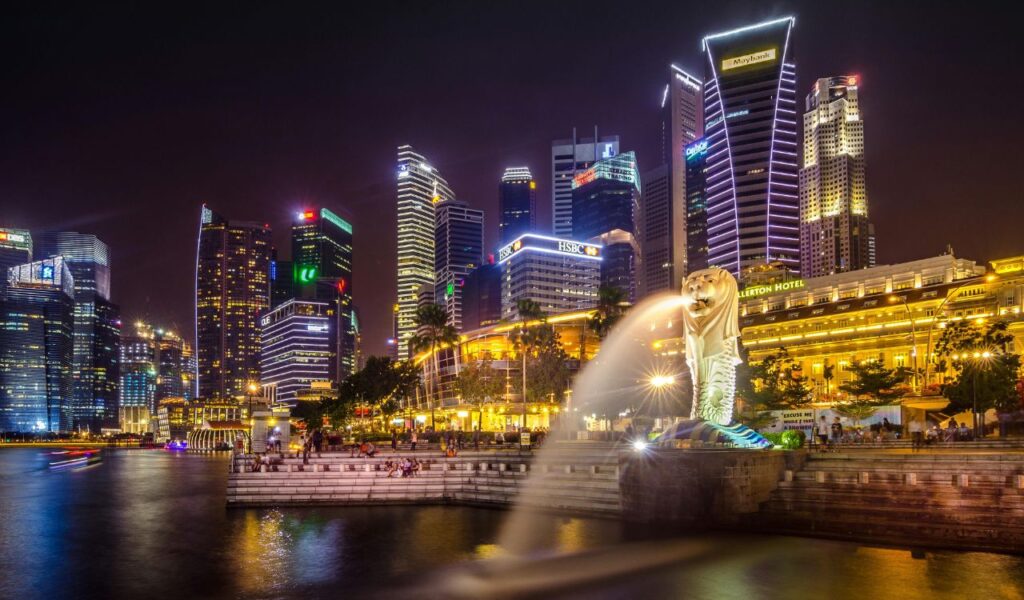 Singapore skyline at night with the Merlion statue and illuminated skyscrapers reflecting on the water.