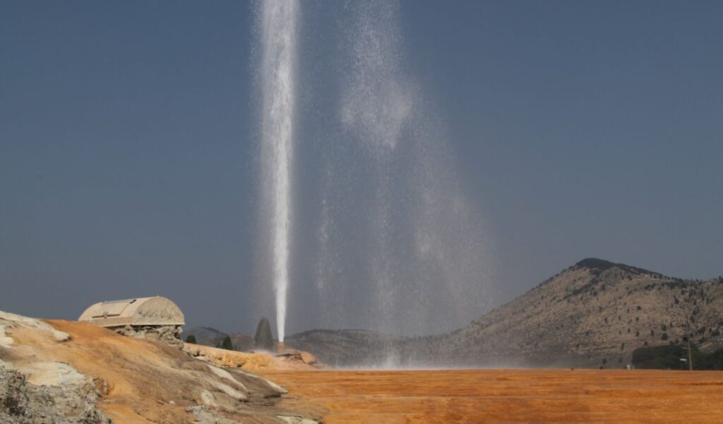 Soda Springs Geyser erupting with water spray against mountain backdrop.