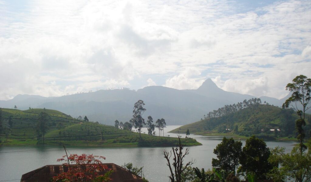 Peaceful lake in Sri Lanka with green hills, trees, and misty mountains in the background