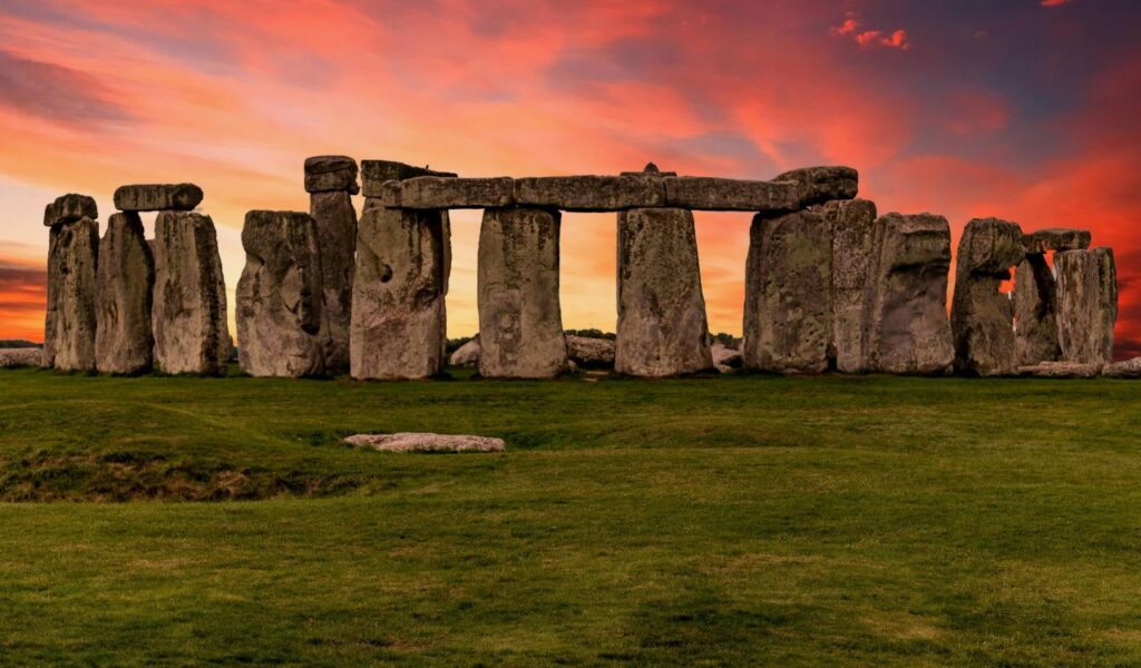 Stonehenge in England with large standing stones arranged in a circle, set on grassy plains under a vibrant sunset sky.