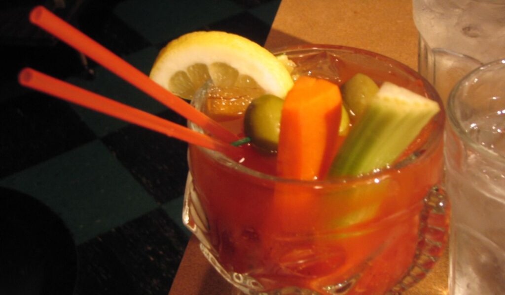 Bloody Mary cocktail garnished with celery, carrot, lemon, and olives, served with two straws