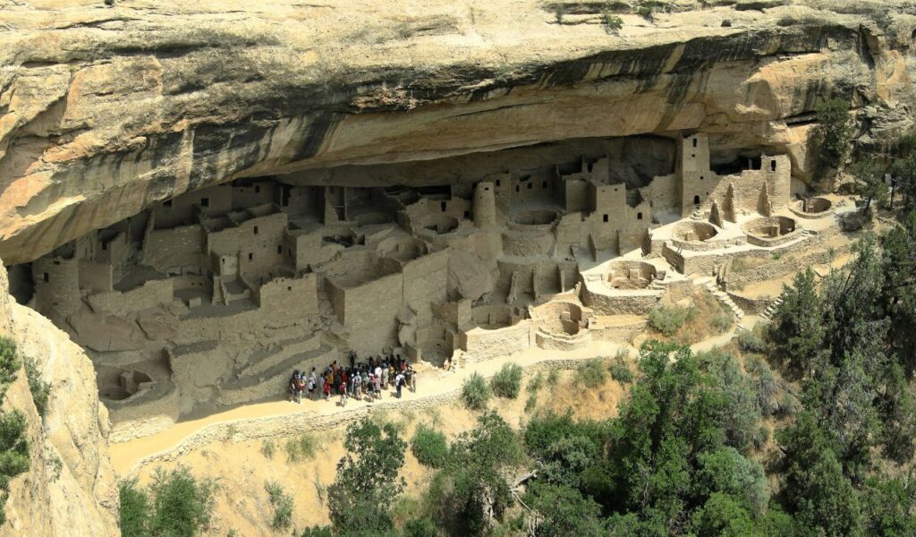 Cliff dwellings at Mesa Verde National Park in Colorado, showing circular kivas and stone structures beneath a rock ledge.