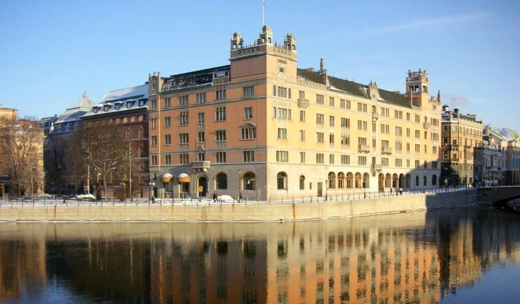 Historic government building in Stockholm reflected in the calm waters of a canal on a clear winter day.