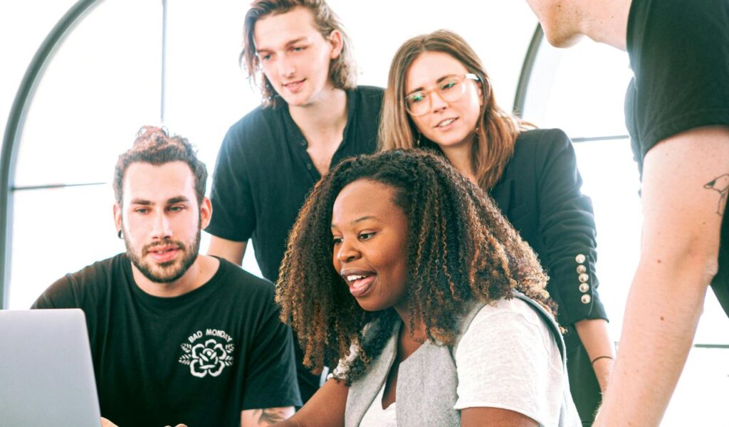 Group of young adults collaborating around a laptop in a bright room