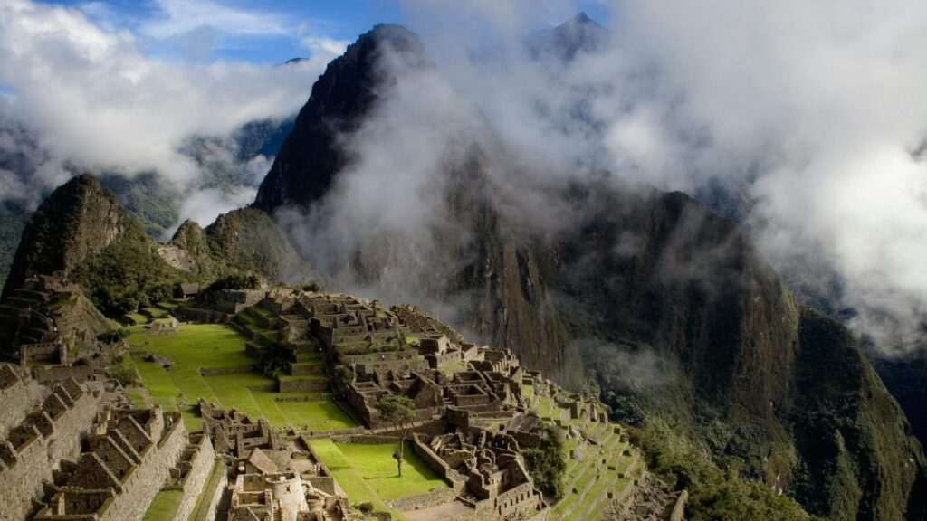 Machu Picchu in Peru surrounded by misty mountains, showcasing ancient Incan ruins and lush green terraces under a cloudy sky