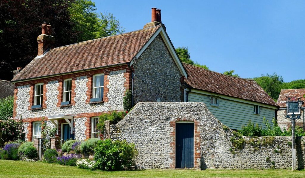 Charming English countryside cottage with red-tiled roof, stone walls, and a lush garden blooming with flowers.